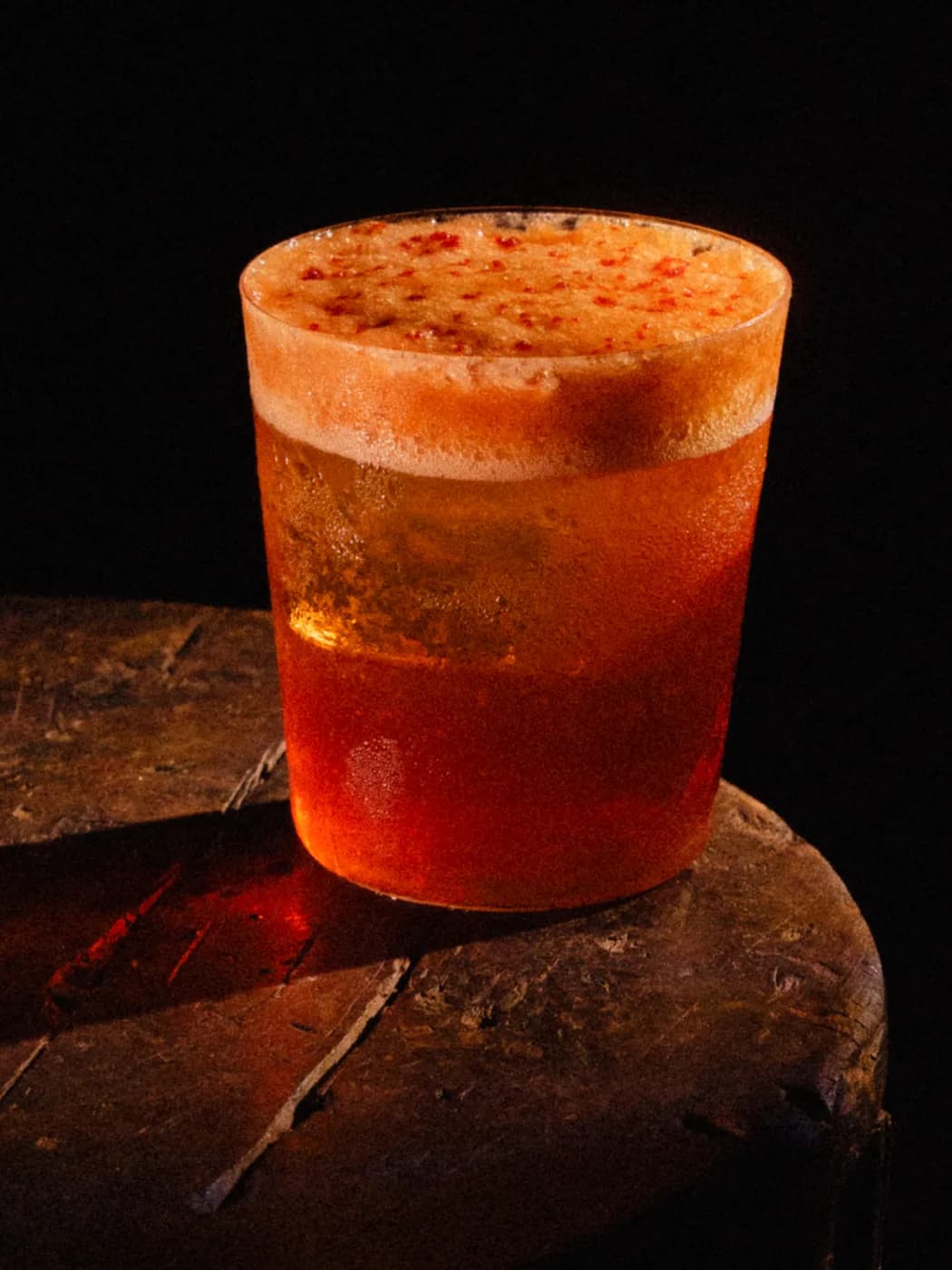 An amber drink with chilli-flecked foam on a worn wooden stool