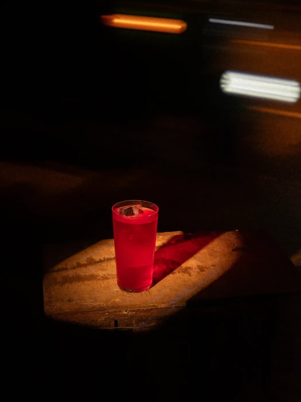 A tall red drink on a wooden block with streaks of passing light behind it