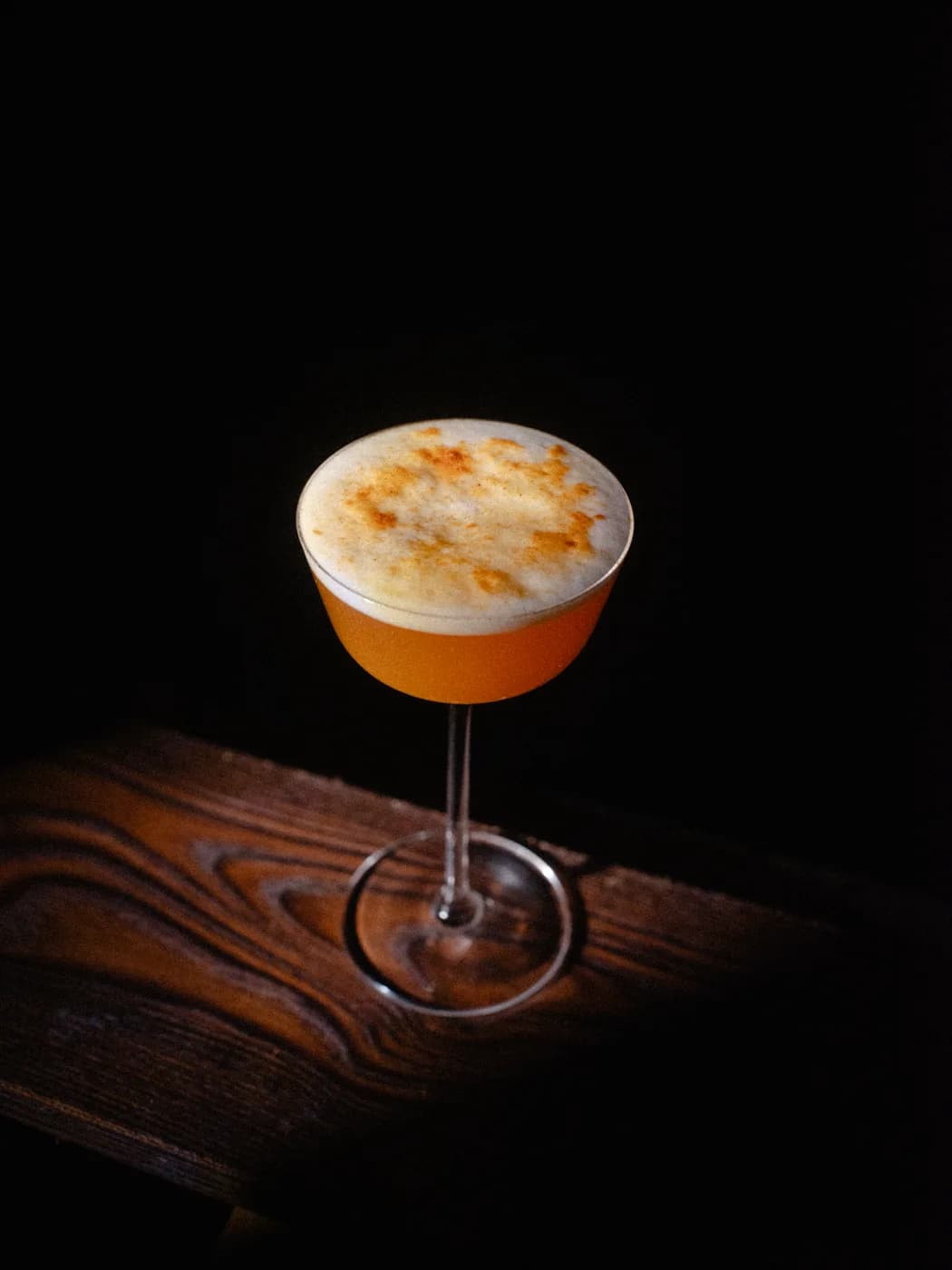 An orange sour in a stemmed glass on dark grained wood