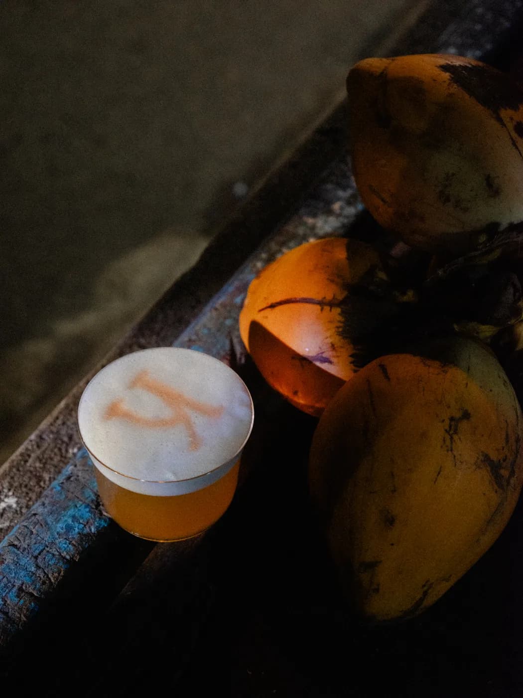 A foam-topped drink on a painted beam next to king coconuts